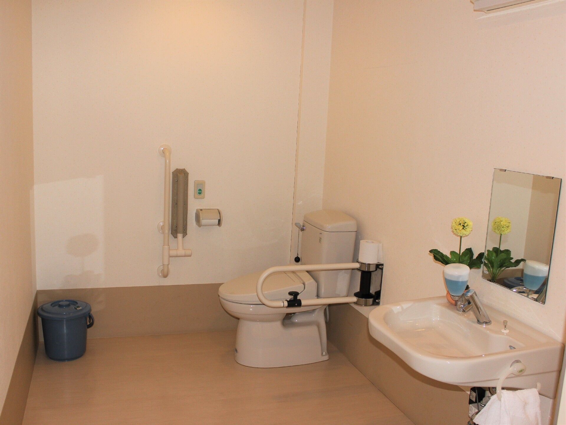 広いトイレには手すりがたくさんつき、ゴミ箱や手洗い場もある。手洗い場には黄色い花も飾られている。