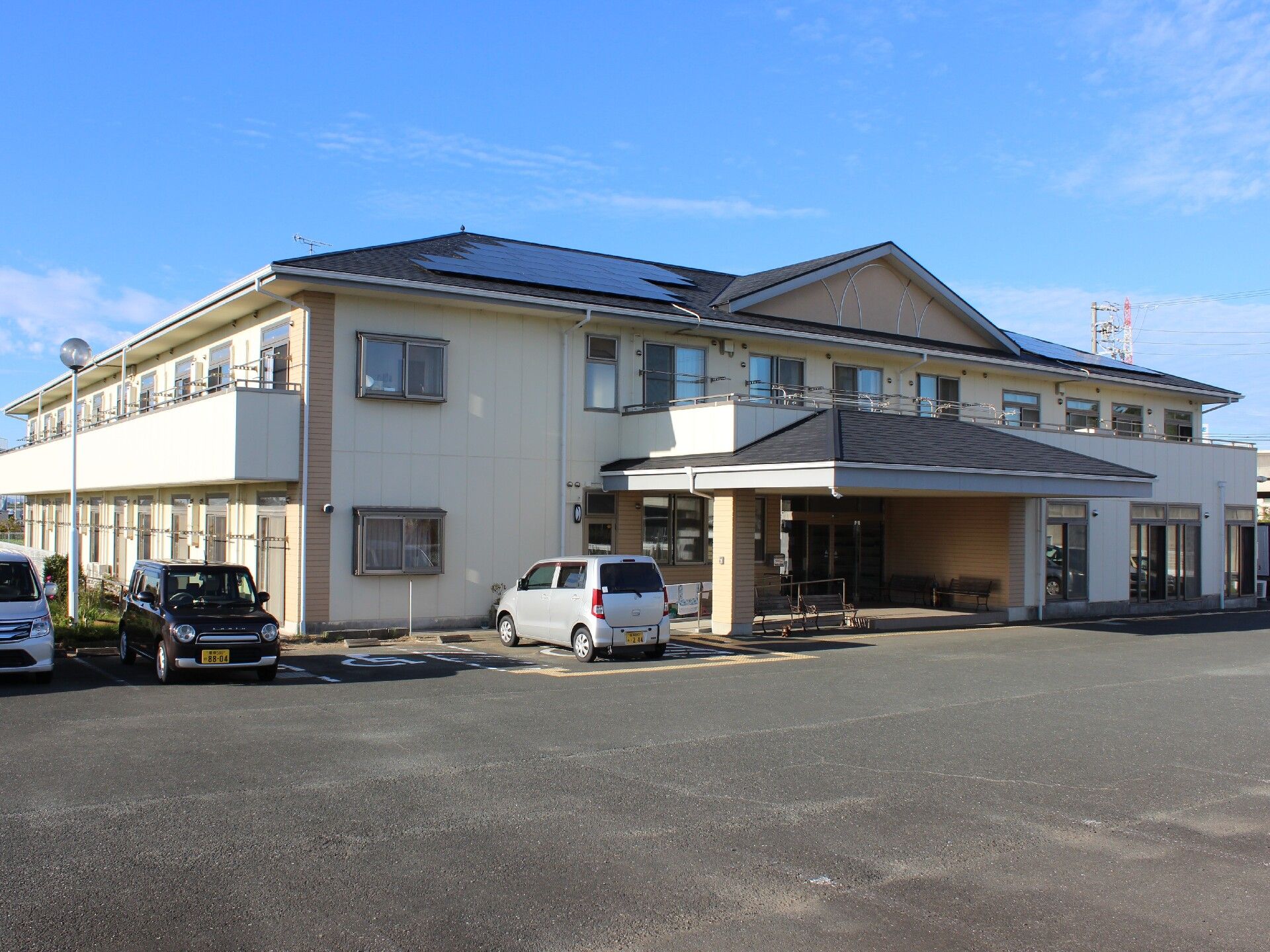 車いすの男性入居者とエプロン姿の女性スタッフが屋外での散歩を楽しんでいる様子。