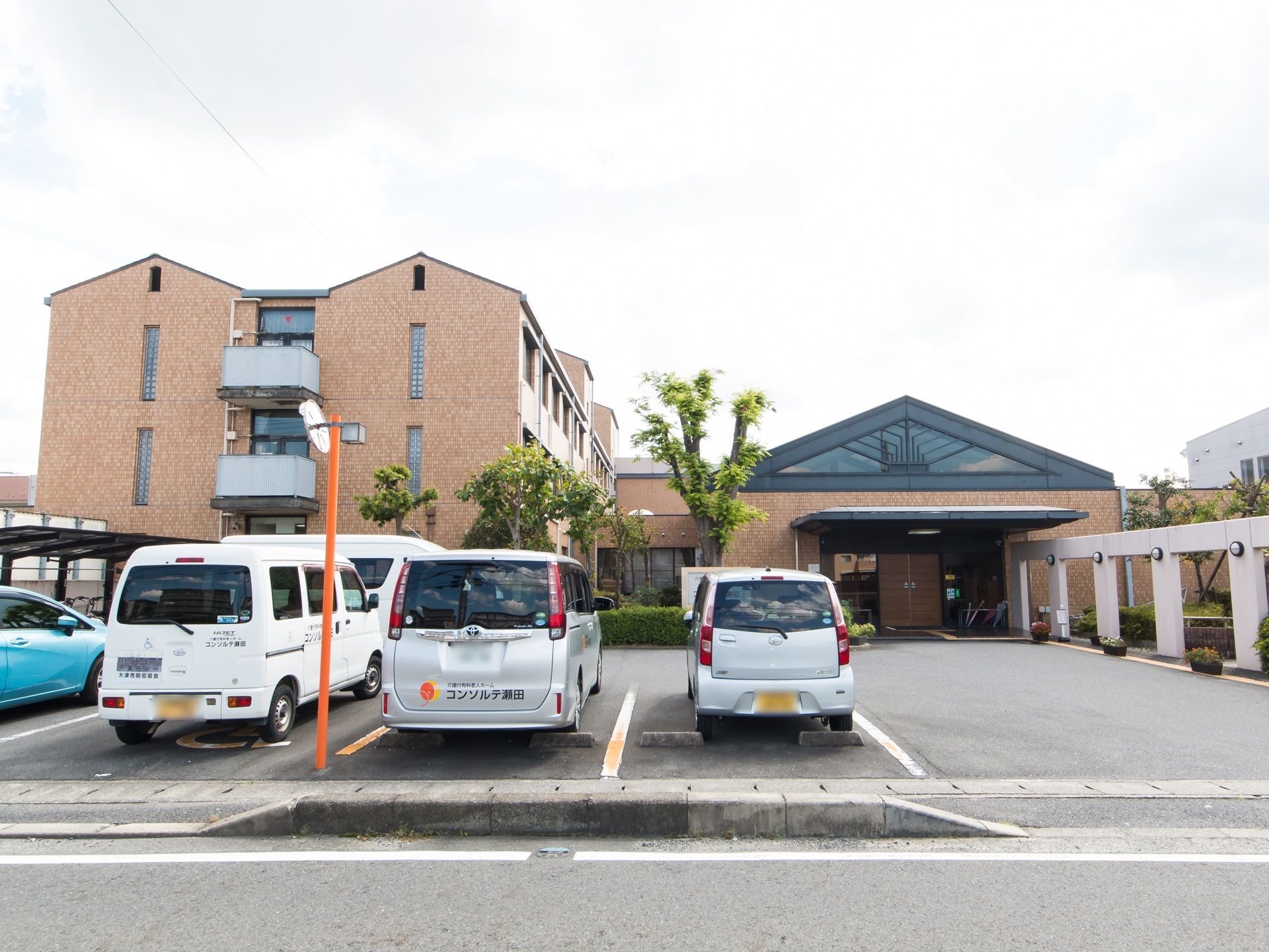 広々とした敷地内に、駐車スペースが多数確保されている。送迎用に施設の車も用意されている。エントランスの前は、通路としてスペースが空けてある。