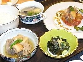 洋風のメインの料理にわかめのおひたし、白いご飯、根菜の煮物、スープなどが並んでいる。