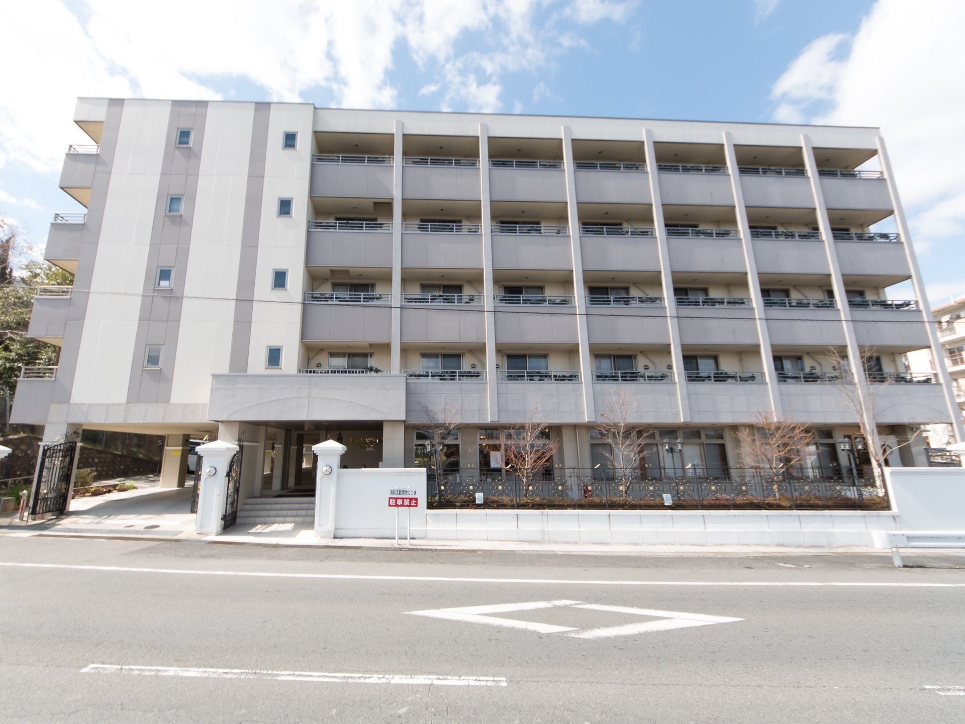 ５階建ての鉄骨造りの建物が道路に面している。施設の周囲には白い塀が設置されており、植栽が施されている。