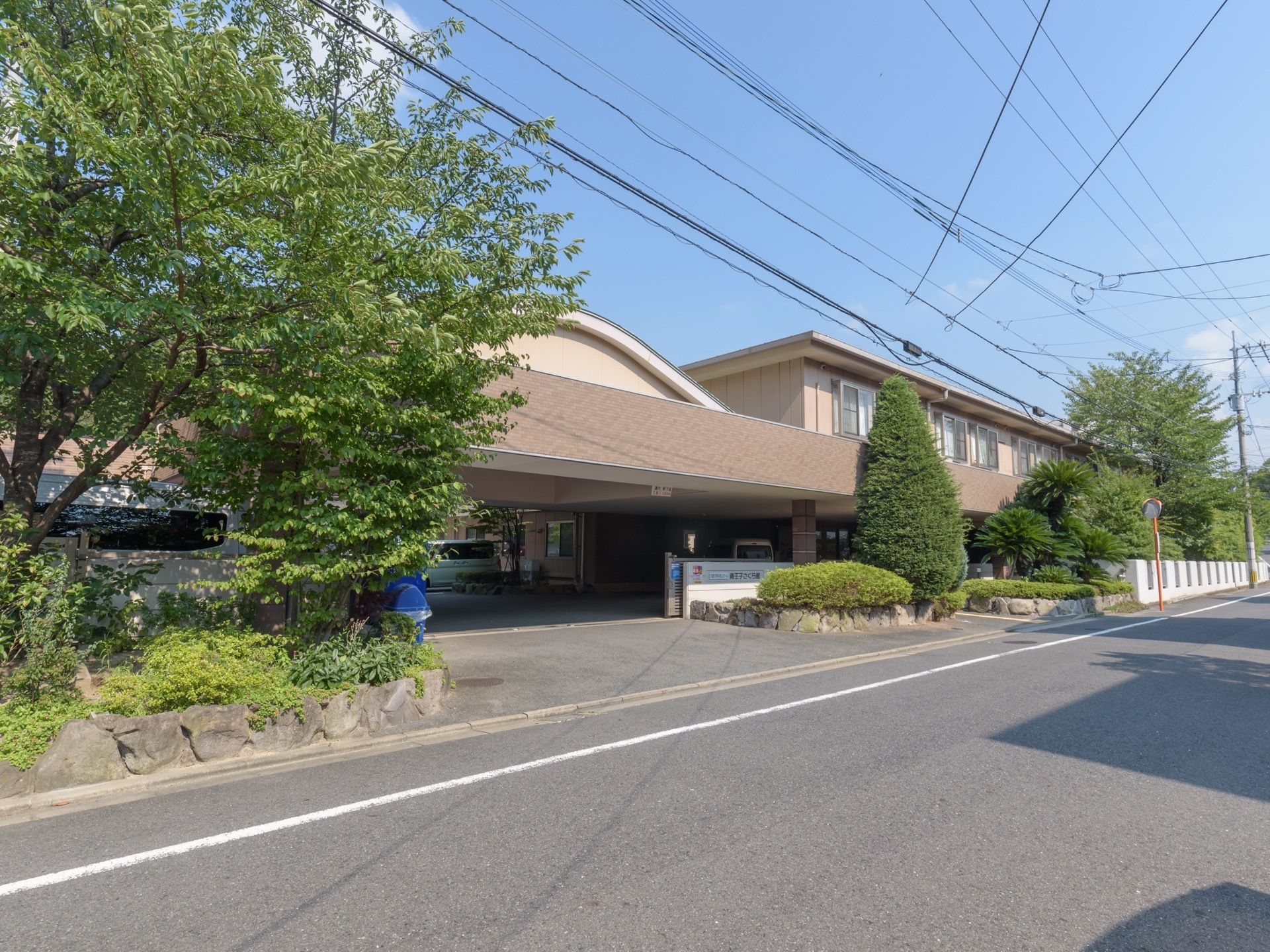 施設の前には道路があり、まわりには木が植えてある。敷地内への入口は大きく、玄関上には屋根が付いている。