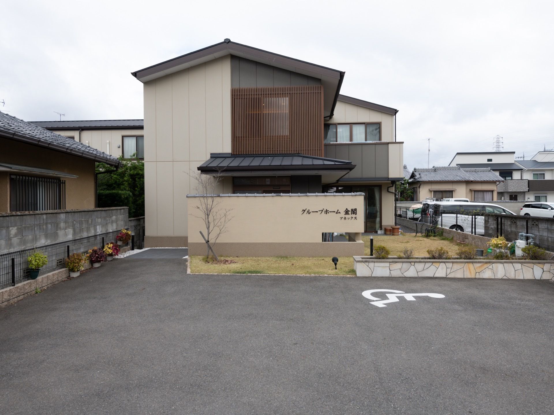 車椅子専用駐車場が、施設の前に設置されている。まわりは住宅街である。アスファルトの敷地が広がっている。