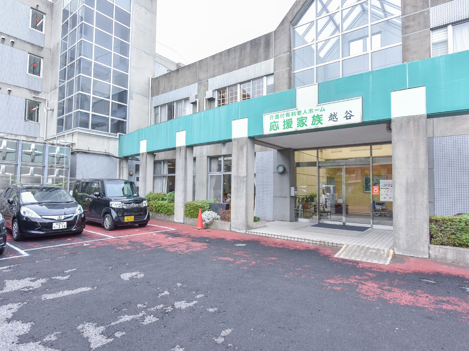 施設の前面はガラス窓になっており入り口付近に看板がついています。目の前は駐車場になっており何台も車が停まっています。