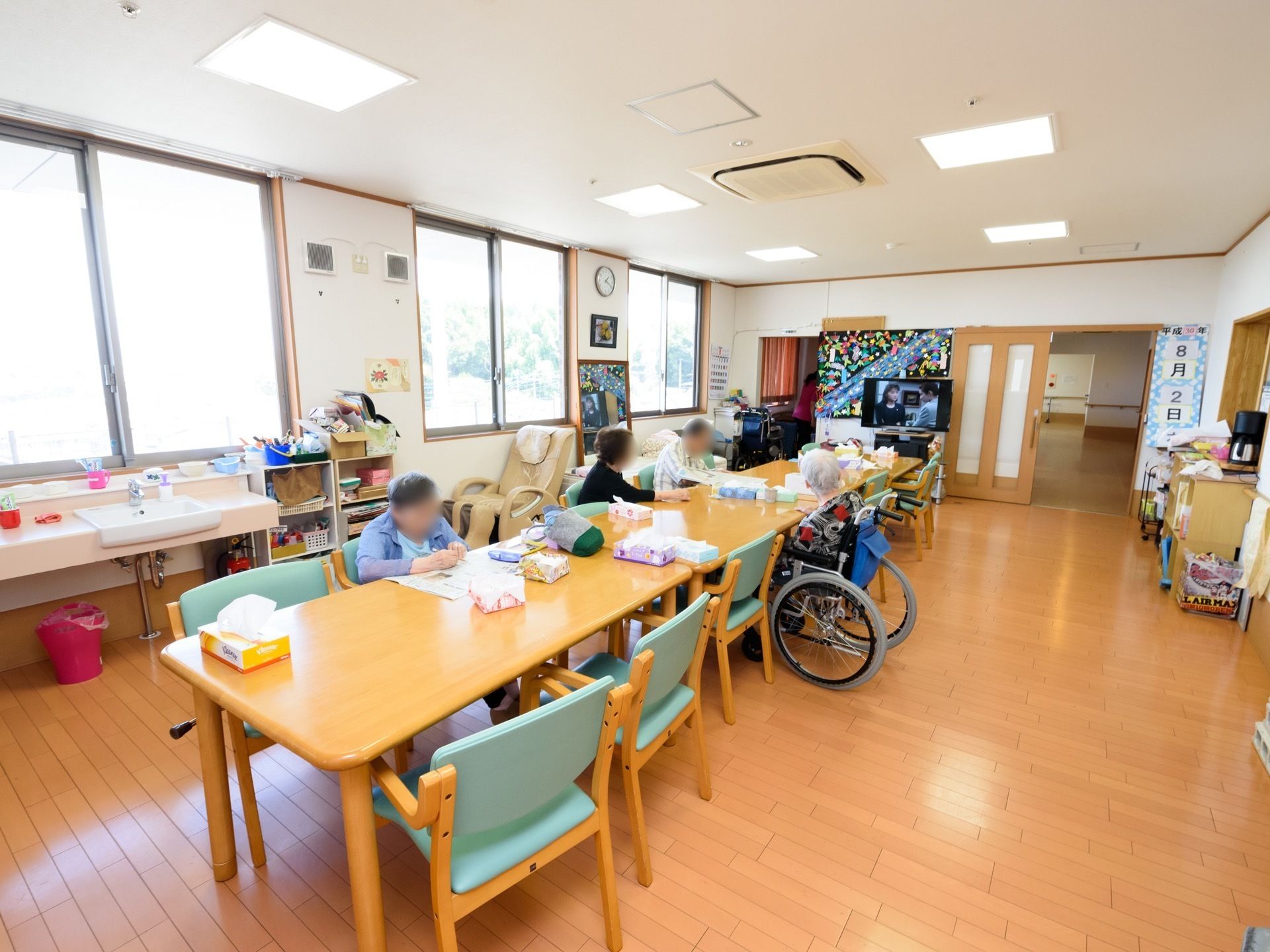 入居者様が椅子に座って、それぞれ思い思いの時間を過ごしている。洗面台の下に消火器やごみ箱が置かれている。