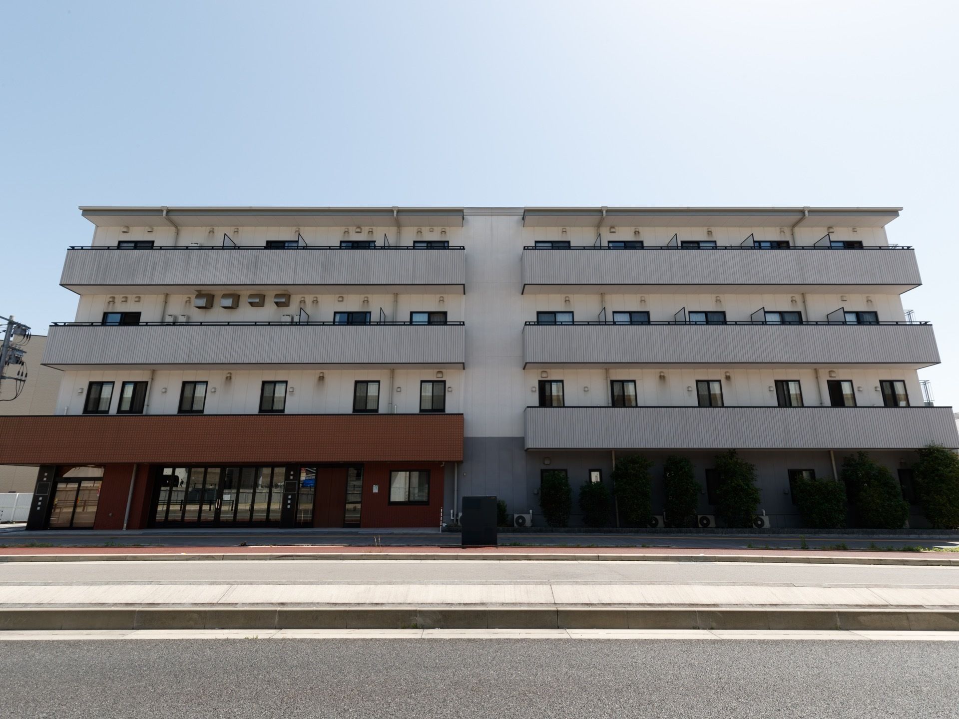 施設の建物は鉄骨造りの4階建てである。白色壁の建物でベランダが付いている。建物の前面に高速道路下の道路が見える。