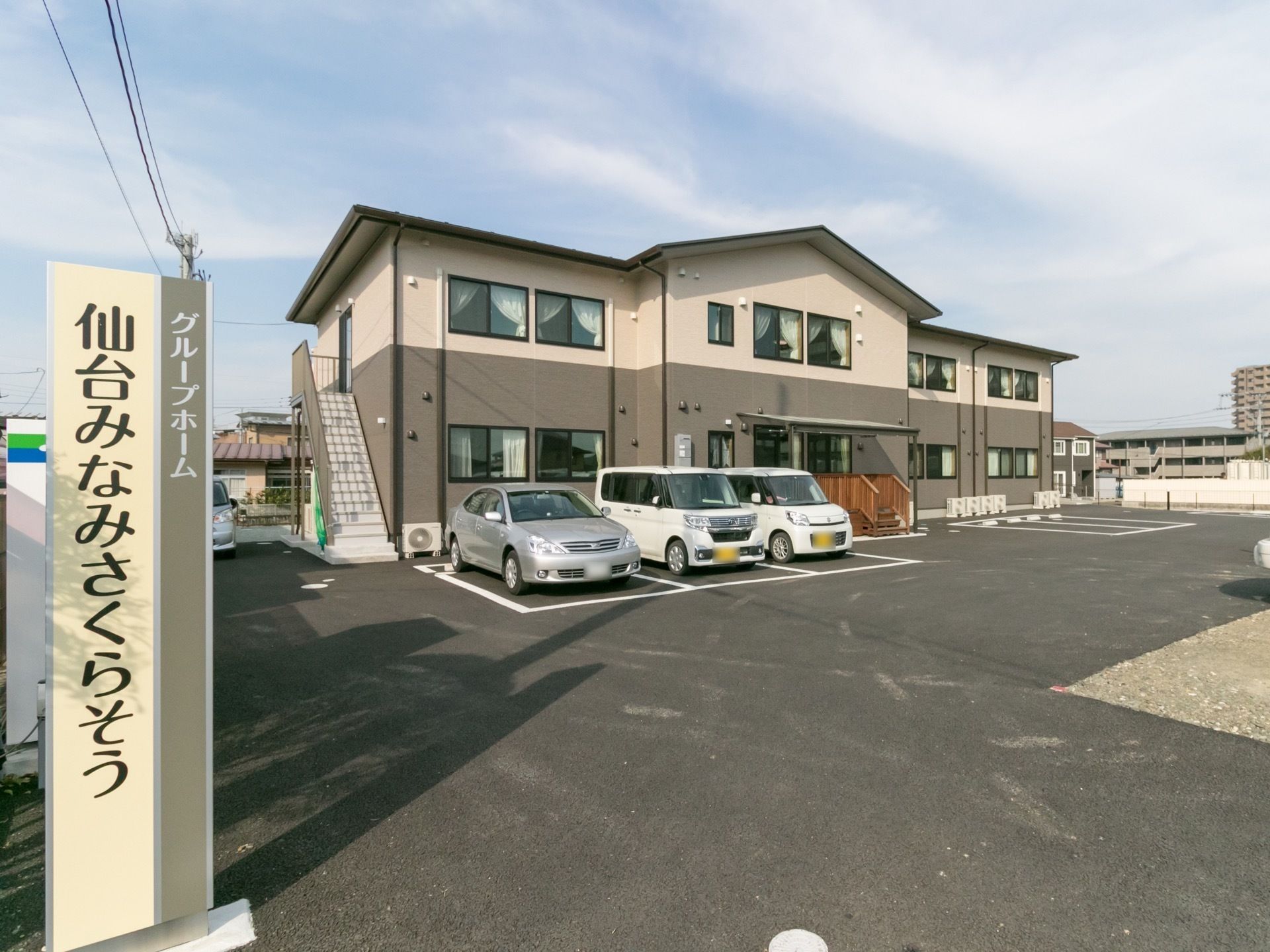 広々とした敷地内に２階建ての施設が建っている。ウッドデッキが１階に設けられており、２階部分から外階段が設置されている。