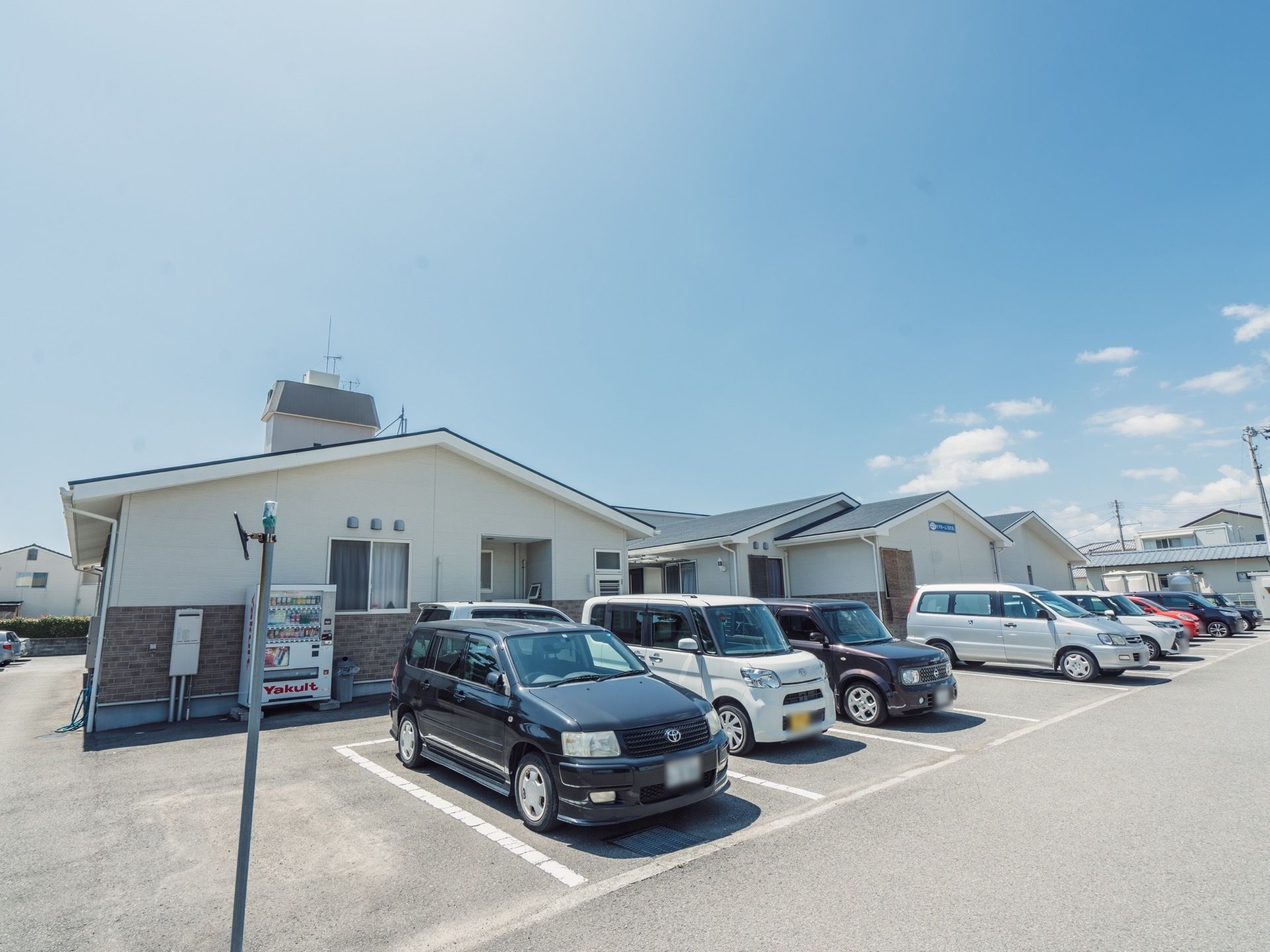 建物の前に駐車スペースが多く完備されている。辺りは広々としていて、アスファルトで整地されフラットである。