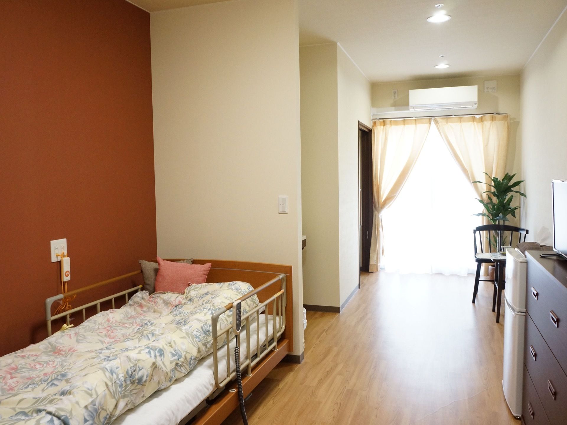 白を基調とした洋風の部屋づくりである。白いカーテンから覗かせた窓から、部屋に光が差し込んでおり、その上にはエアコンがついている。