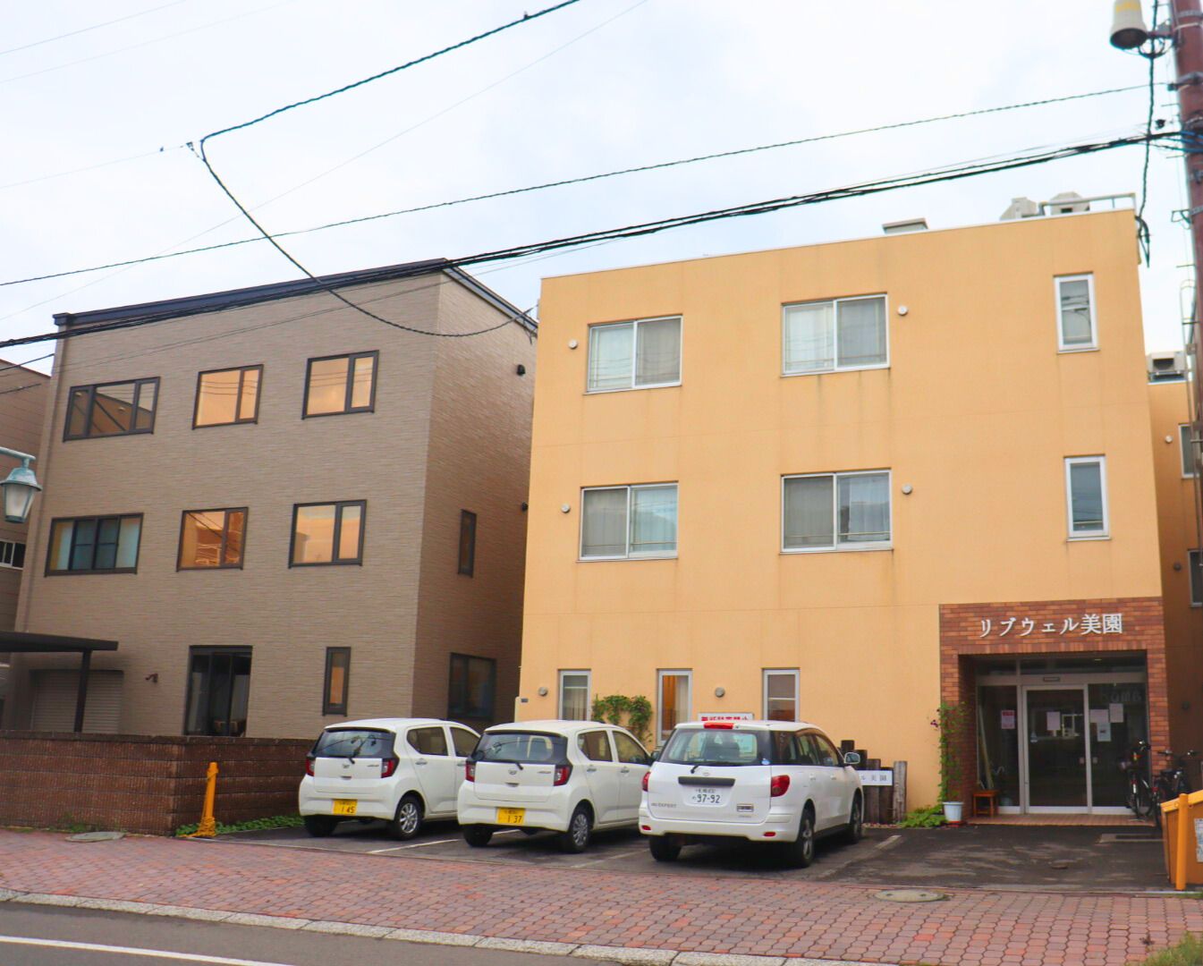 施設は３階建ての凹凸の無い四角い建物である。１階の入り口部分はレンガ調に装飾されている。建物の前に車が停められている。