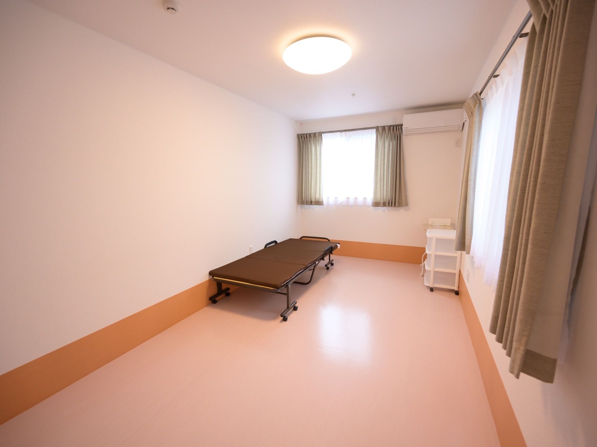 洋室のお一人様用の居室で、室内には二面に窓があり、カーテンが備わっている。ベッドが置かれ、エアコンの設備がある。