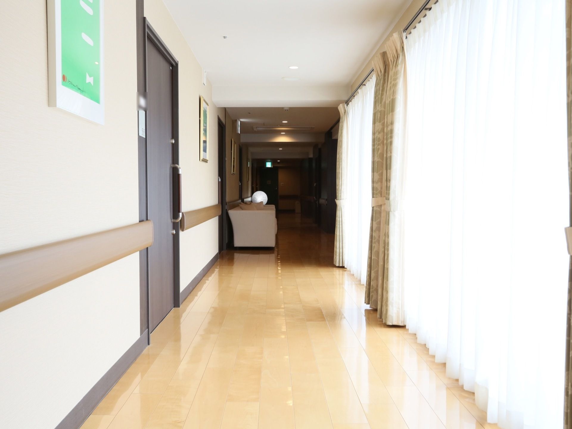 通路はとても明るく、床はきれいに掃除されて光沢がある。左側の壁には茶色い手すりが設置され、上の方には絵が飾られている。
