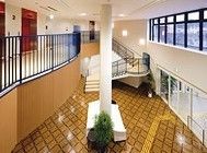 吹き抜けの１階から２階へ向かい、緩やかな傾斜の階段が繋がる。２階には赤い扉のエレベーターが２基ある。