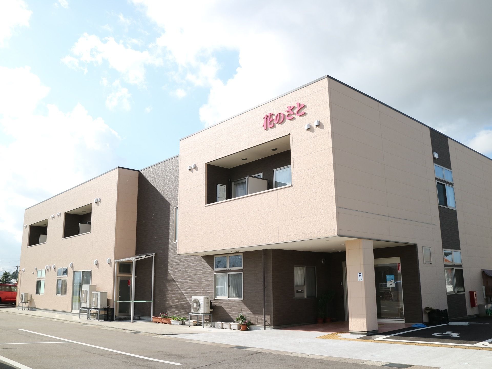 ツートンカラーにあしらわれた、２階建ての施設である。エントランスには屋根が設けられている。駐車場もある。