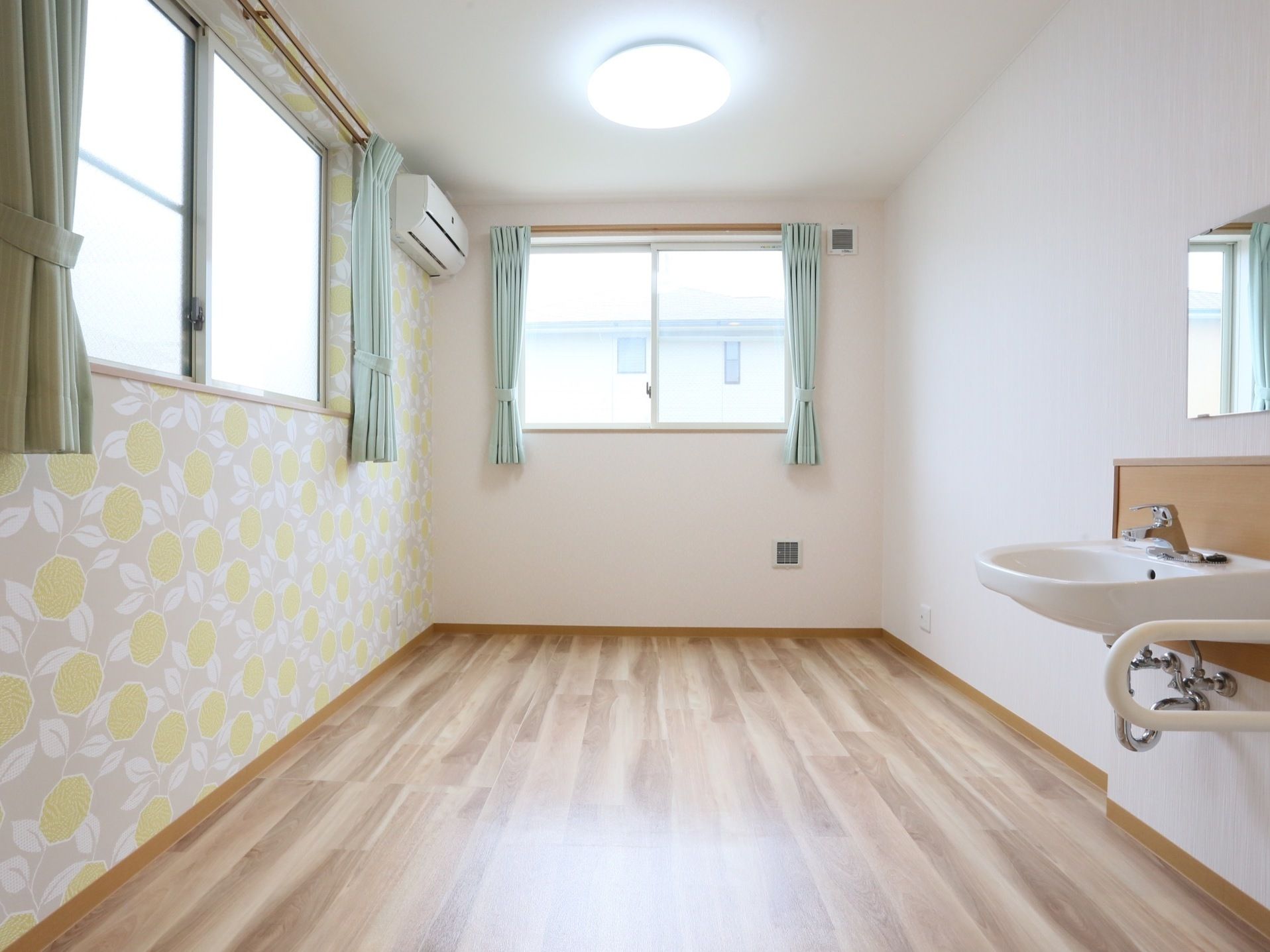 床は木目調になっており、左側の壁紙は花の模様になっている。腰高の窓が2か所ついており、グリーンのカーテンが掛けられている。