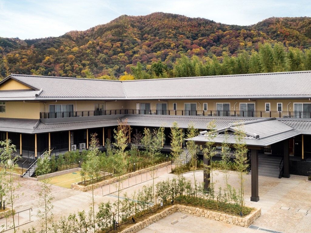 色づき始めた山をバックに立地している、２階建ての施設の外観
