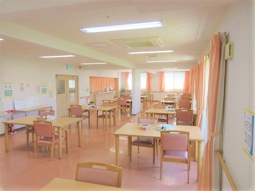 複数の窓が設けられた開放的な食堂である。あたたかみのある淡いピンク色のカーテンが備えつけられている。間隔をとってテーブルが並べられている。