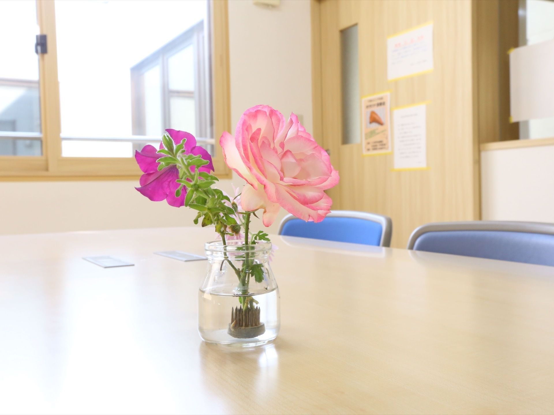 テーブルと椅子が設置されている。テーブルの上に置かれた透明の花瓶には、ピンクと白色の花と、鮮やかな紫色の花が活けられている。