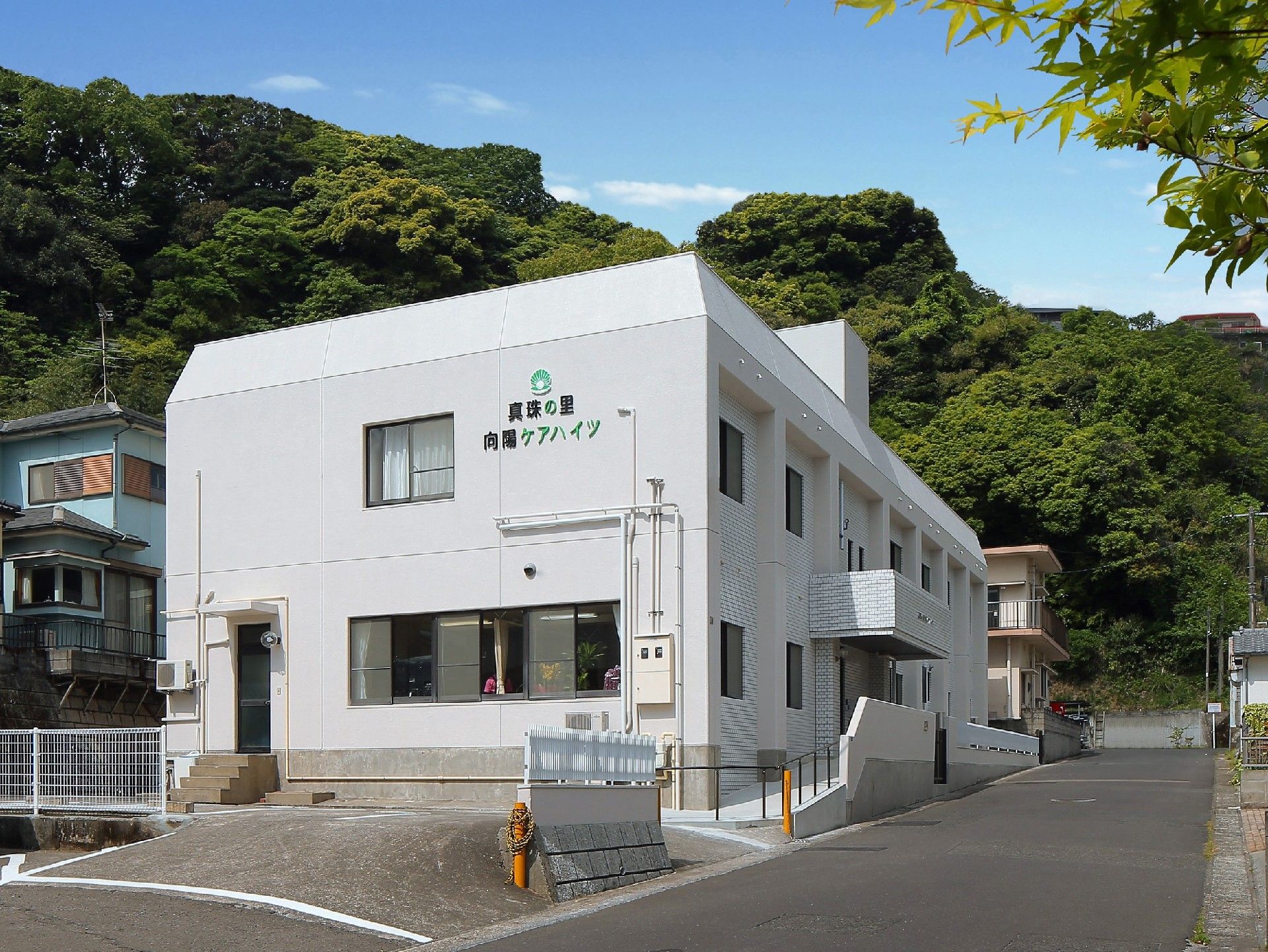 白い壁と奥の山のコントラストが印象的な写真。施設の外観写真