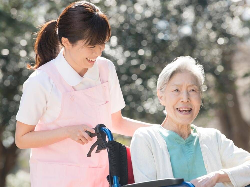 車椅子で散歩をする高齢女性と付き添いの女性ヘルパー
