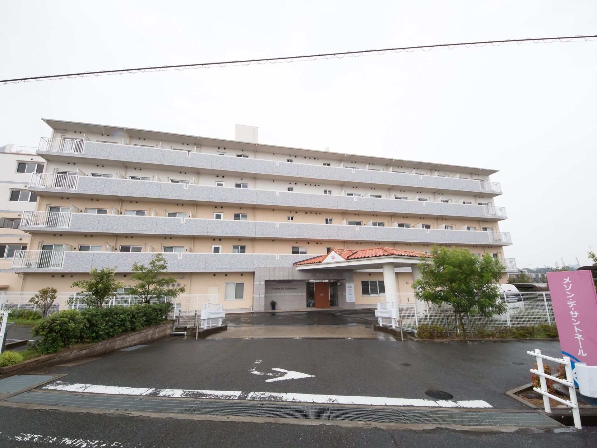 施設は５階建てで、敷地内には広い駐車スペースが設けられている。玄関前には、オレンジ色の屋根も設置されている。