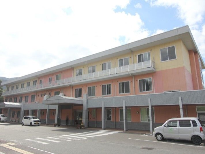 3階建ての建物は横に長く、玄関には車寄せが付いている。駐車場もあり、車も止まっている。