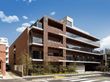 現代的な鉄骨造りの4階建ての建物。周辺には緑が植えられ、各フロアにはベランダもついている。