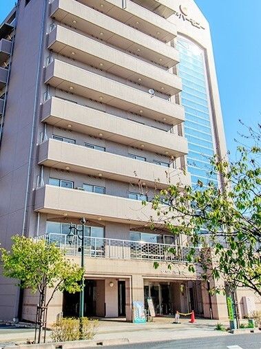 9階建ての薄茶色の外壁のマンション。前には木があり、スタイリッシュに仕上がっている。