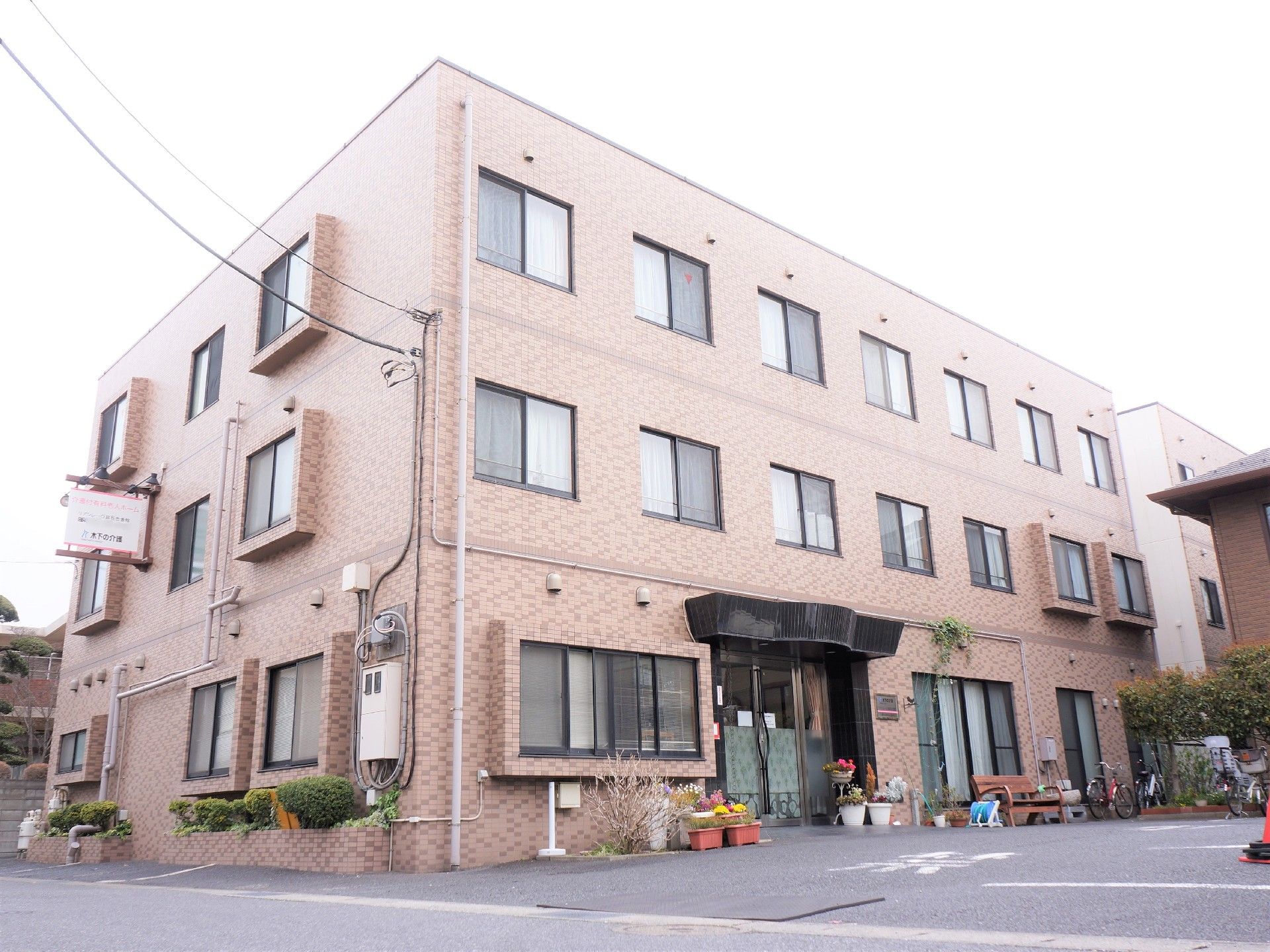 当施設は、茶色い3階建ての建物である。周りには、花や植物を植えている。すぐ目の前が駐車場となっている。
