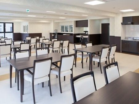 4人掛けのダイイングテーブルが複数置かれた食堂。テーブルセットもキッチンもすべてモノトーンでまとめられている。