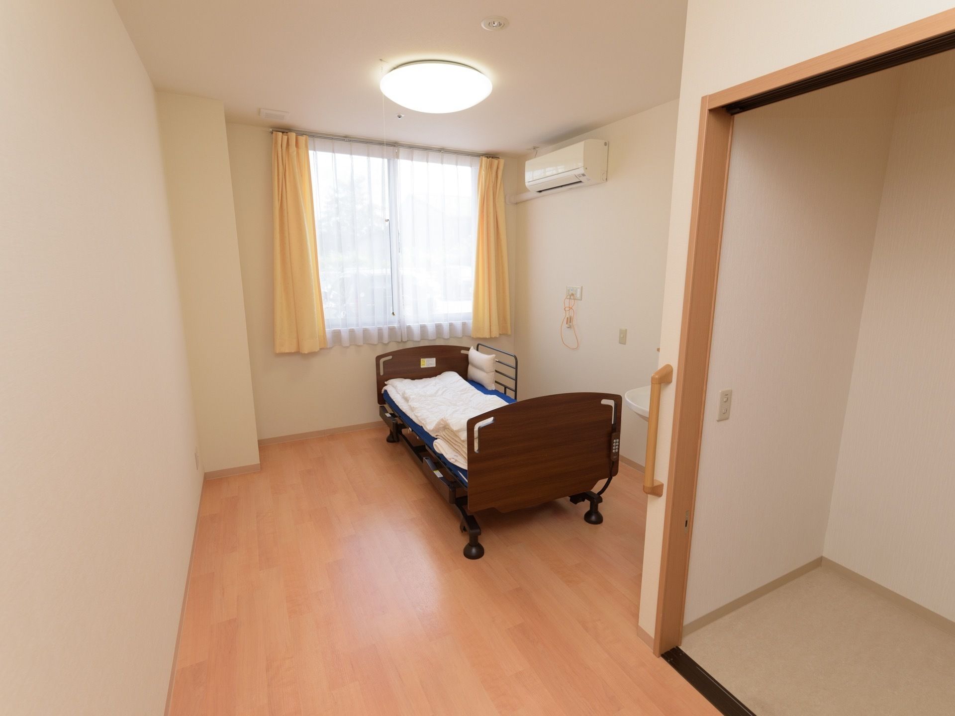 居室の奥にある窓からは日が入り、室内を明るく照らしている。ベッドサイドの壁にはナースコールが設置され、緊急時にはスタッフを呼ぶことができる。