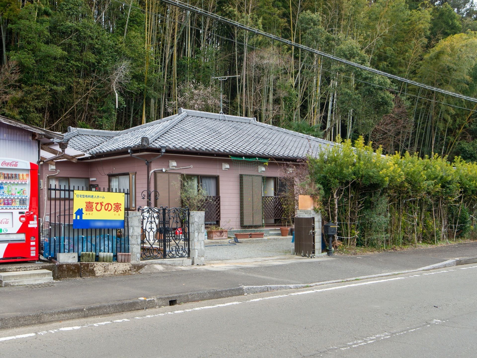 平屋の一軒家で、出入口には施設名が書かれた看板が柵についている。施設の周りには、たくさんの竹が生えている。