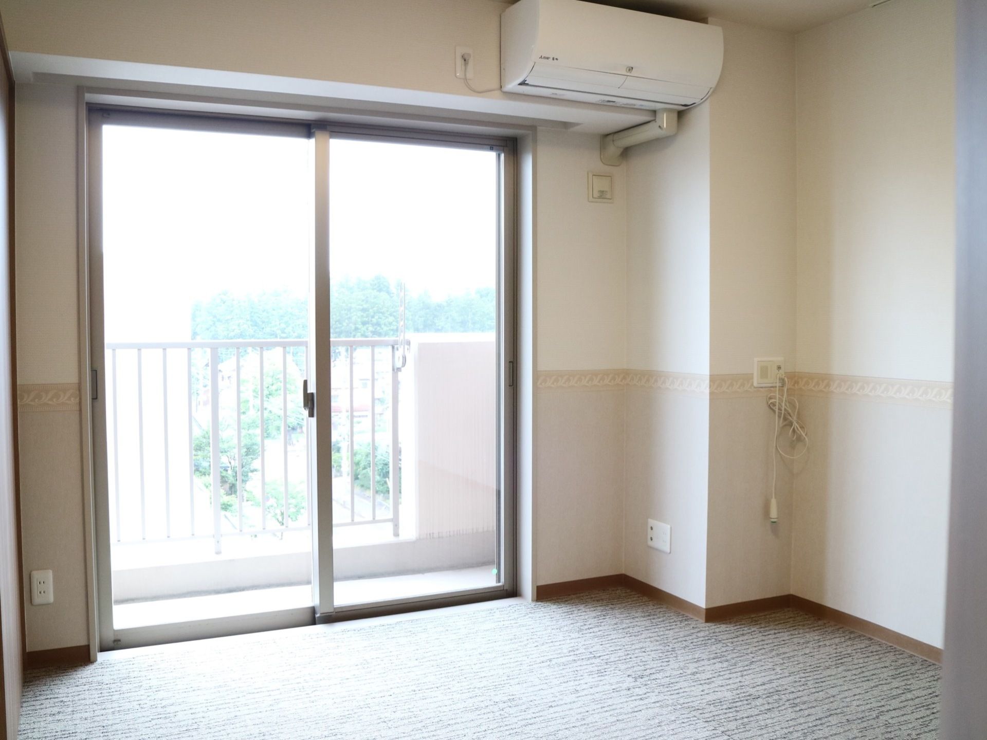 白とベージュの壁の個室で、色の境目に花柄のラインが入っている。ベランダへと出られる大きな掃き出し窓がある。