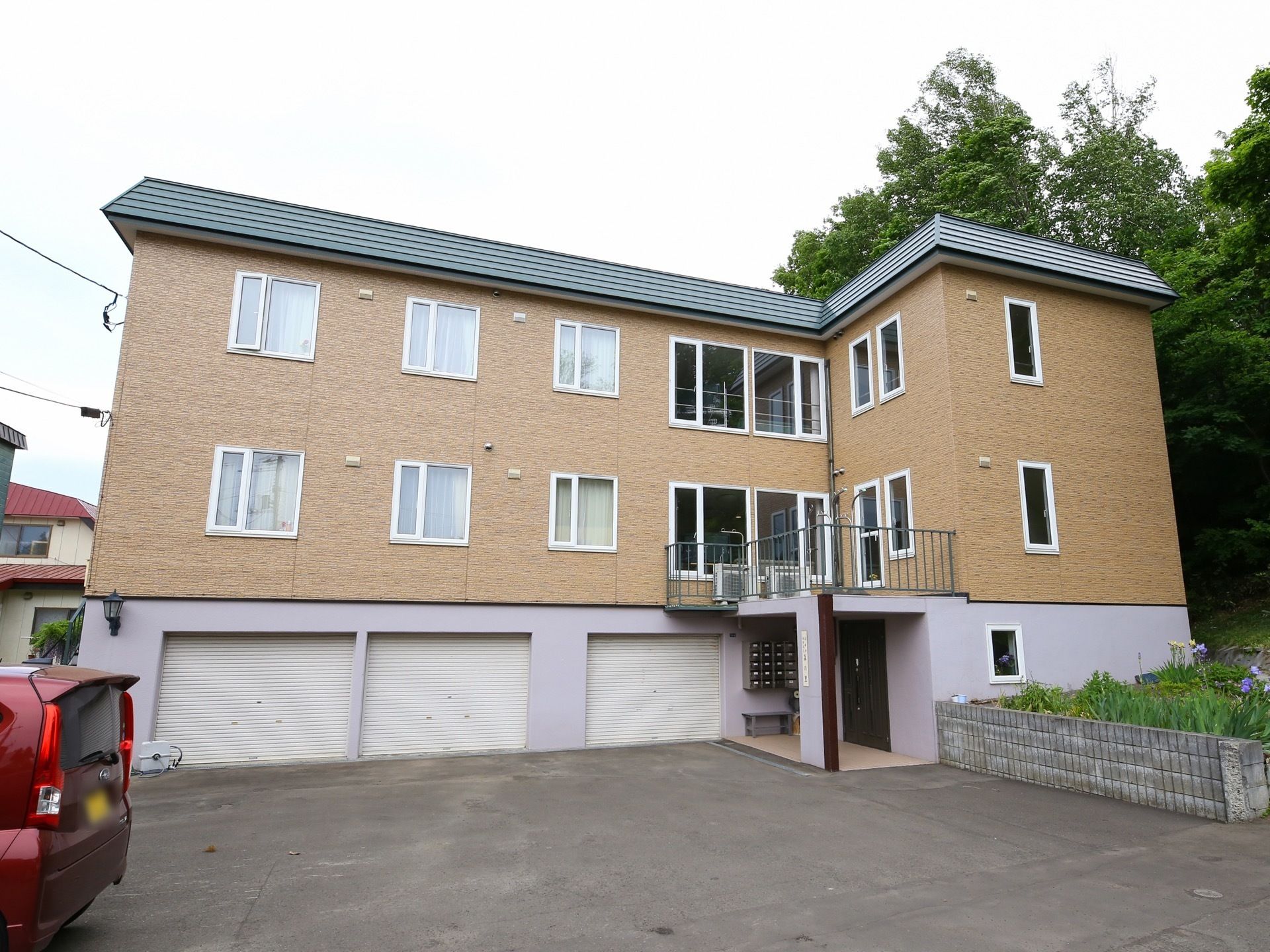 施設は3階建てで1階部分にはガレージがある。2階と3階の外壁はベージュ色である。玄関入口横にはブロック塀で作られた花壇が設置されている。