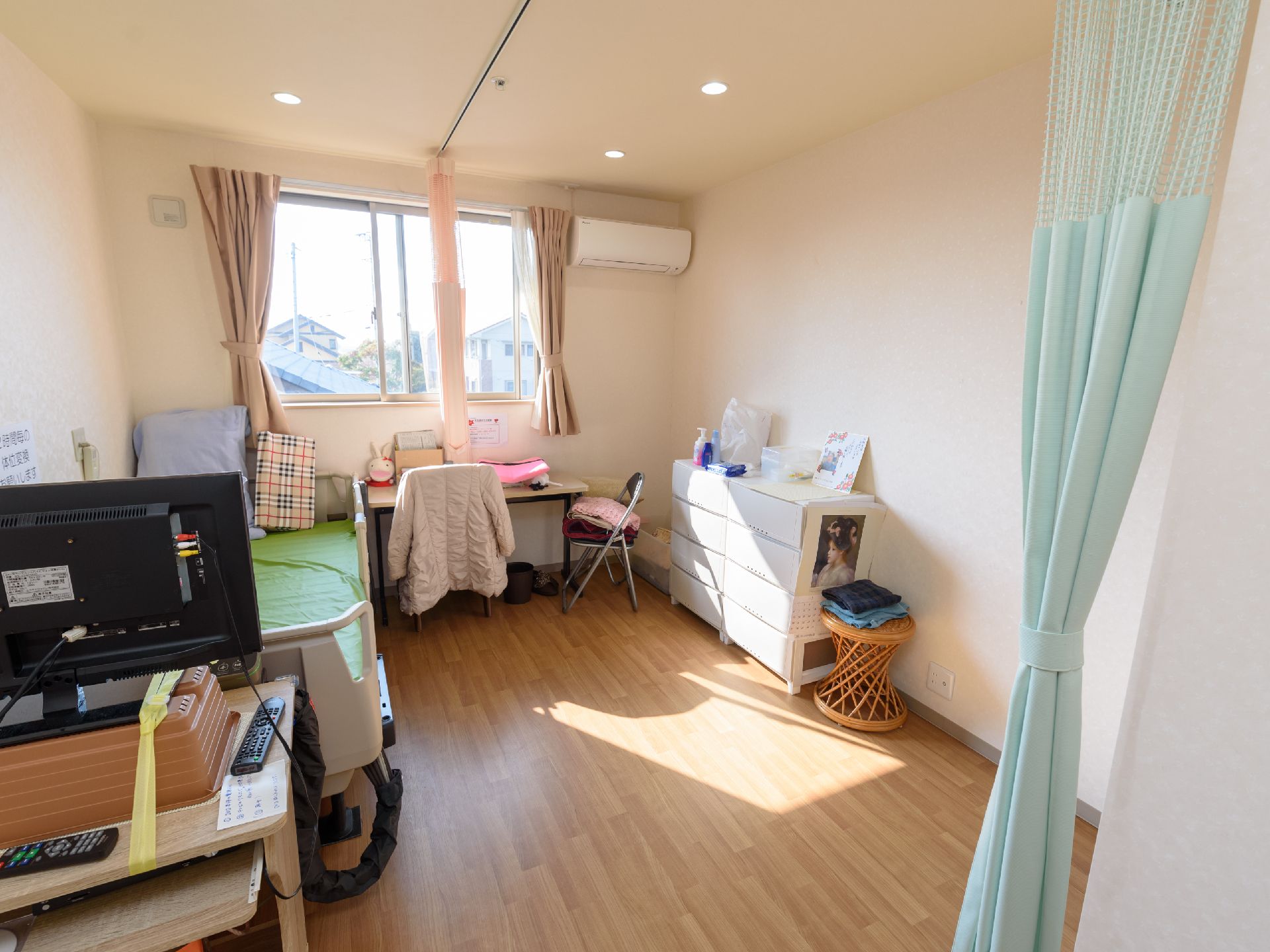 窓側にデスクが設置され、その手前にコートが掛けられた椅子が置かれている。左側の壁にさまざまなクッションが用意されているベッドがある。