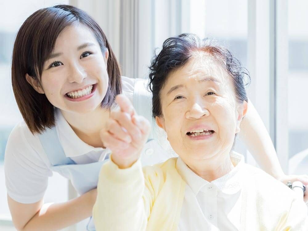 なにかを指さして笑顔で話している車いすの女性とそれを押している介護スタッフの様子