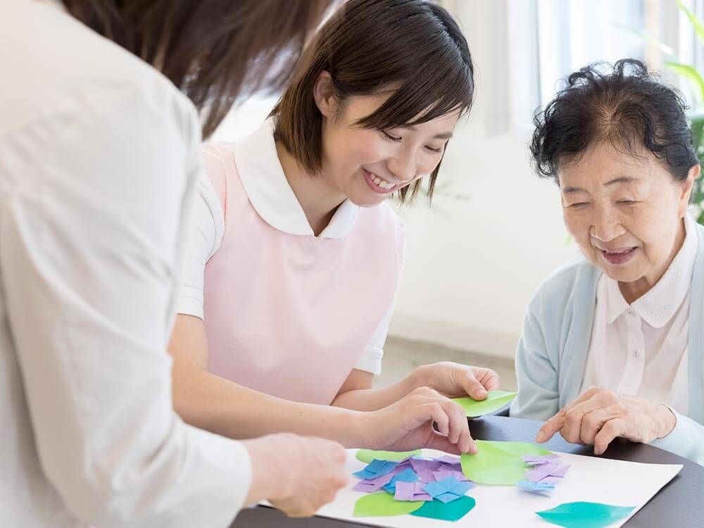 紙を使ったレクリエーションをする高齢女性と指導をする女性スタッフ