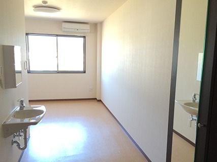 部屋の入り口から奥のほうを写した写真。窓とエアコン、照明などが付いているワンルーム