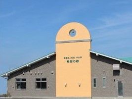 建物を側面から見た様子。ブラウン系の建物には三角屋根が付き、中央には住宅の名前が書かれ、鐘も付いている。
