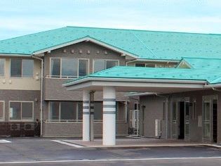 大きな車寄せが付いた２階建ての建物。グリーンの屋根が付き、駐車場もある。