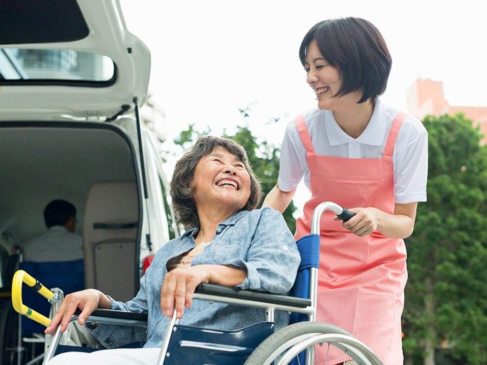 顔を見合わせる車椅子に乗った高齢女性と介助をする女性ヘルパー
