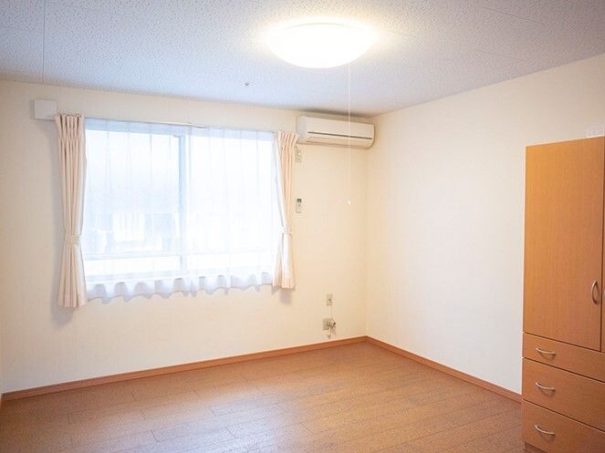 大型の収納家具が付いたフローリングの部屋にはカーテンが付いた大きな窓やエアコンもついている。