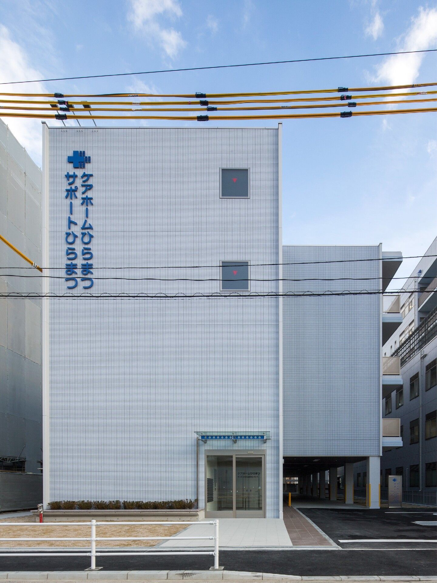 白を基調とした４階建ての建物。外壁にはブルーの文字で住宅名と併設事業所名が書かれている。