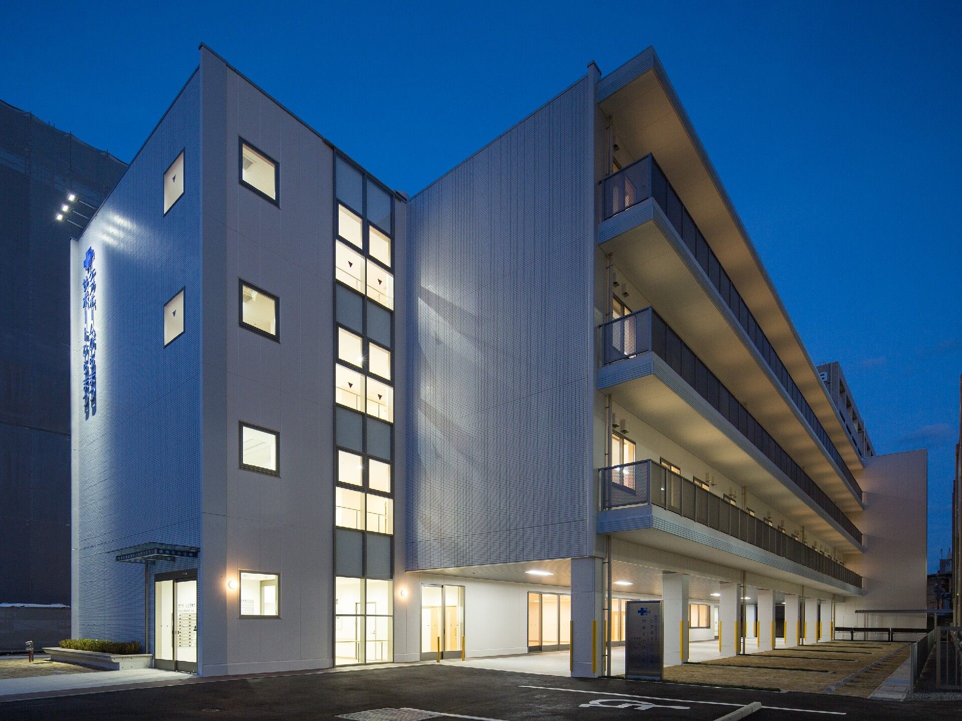 各フロアにベランダがついた4階建ての建物はライトアップされ、外壁には住宅名と併設事業所名が書かれている。