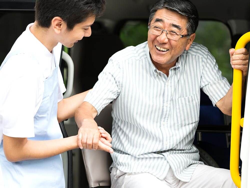 手すりにつかまり車から降りる高齢男性と介助をするヘルパー