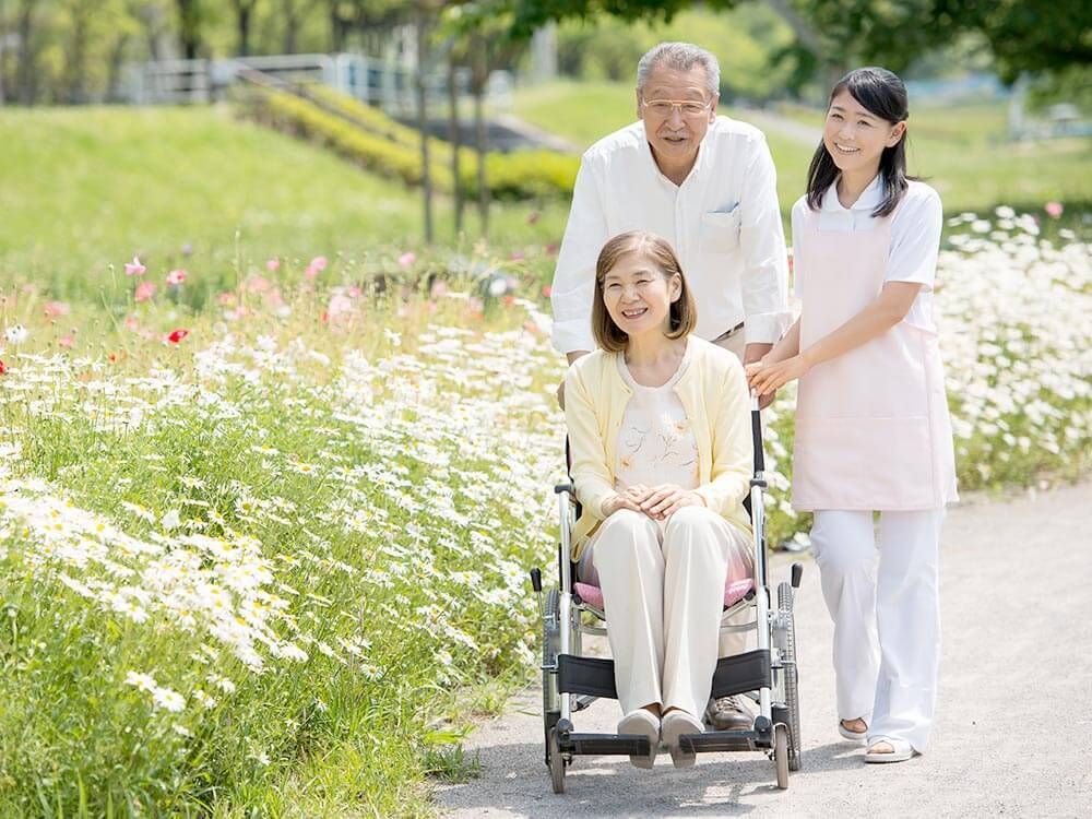 車いすに乗った女性を押す家族の男性とそこに寄り添う介護スタッフの様子