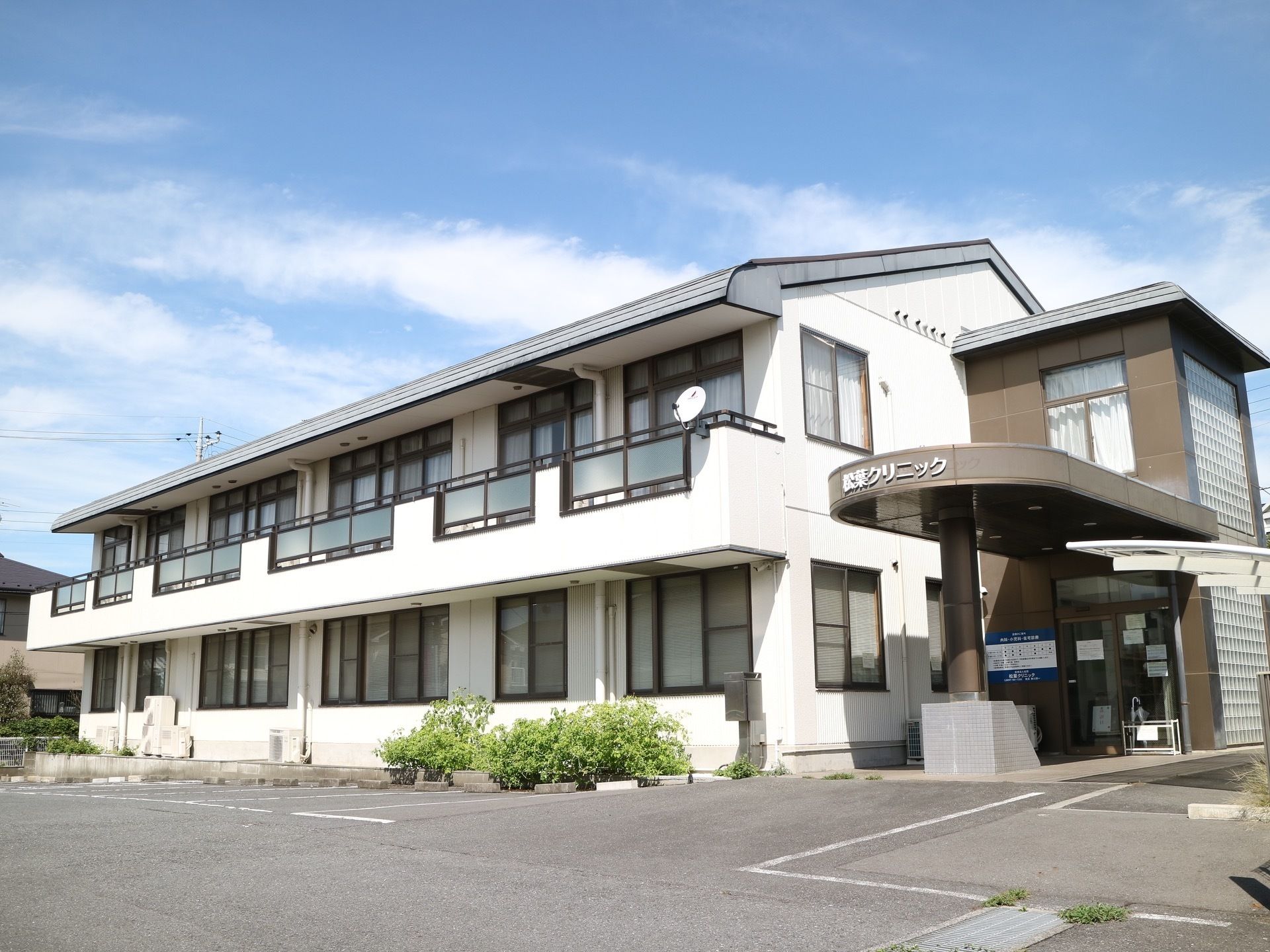 クリニックが併設されている建物。敷地内にアスファルトで舗装された広い駐車場が完備されており、白線が引かれている。