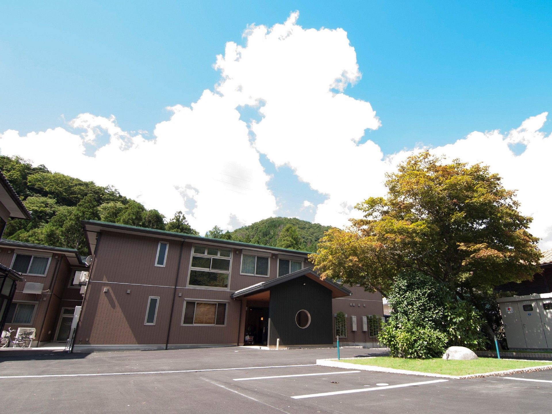 手前に駐車場がある施設の空間。落ち着いた色合いのモダンデザインな建物がある様子