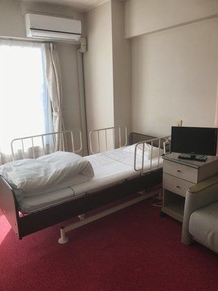 寝具がセットされたベッドが置かれた部屋には、収納棚やテレビ、エアコンもある。