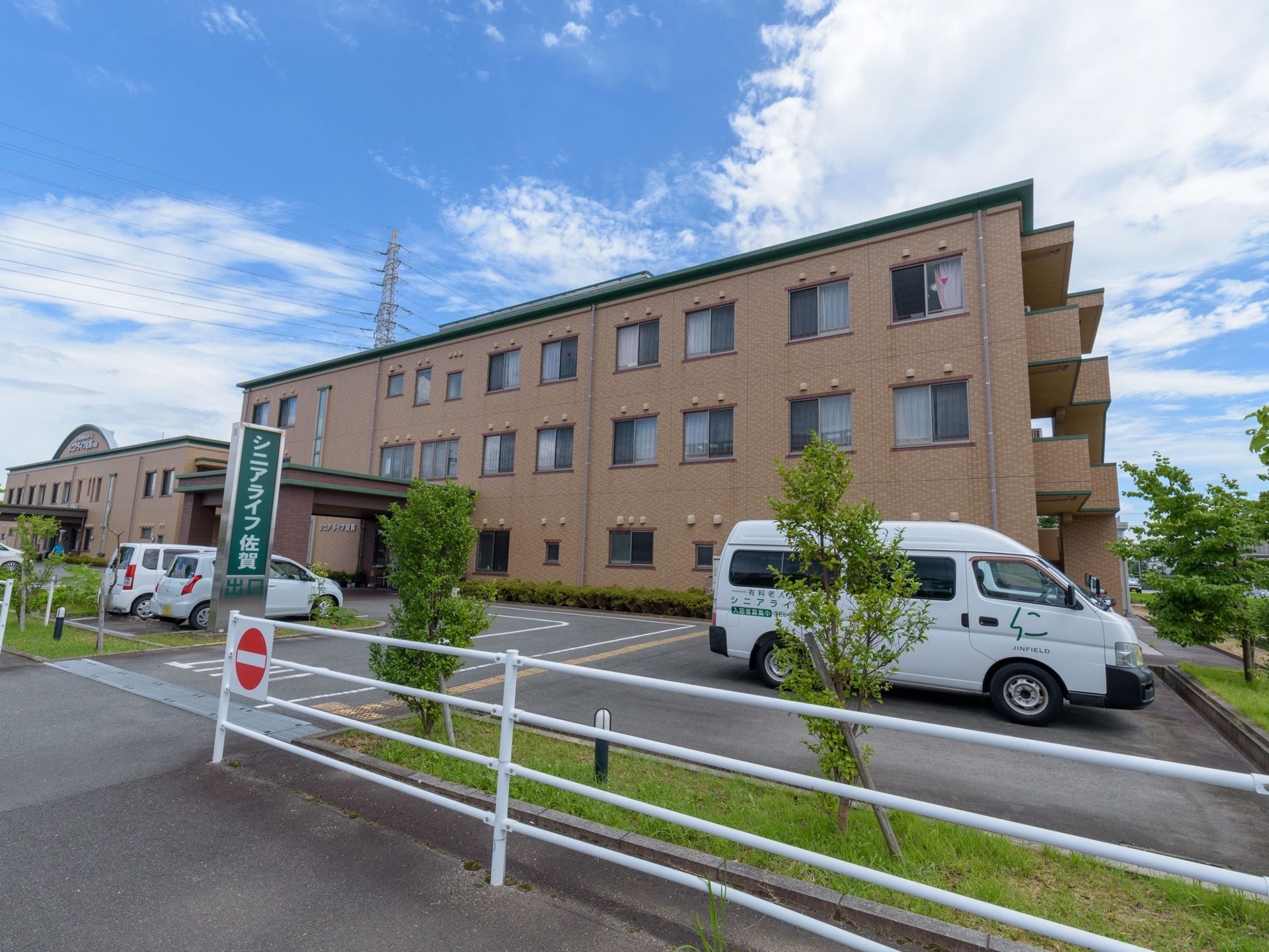 施設内は一歩通行となっている。建物の前には駐車スペースがあり、車が数台駐車してある。施設名が書かれた車も停まっている。